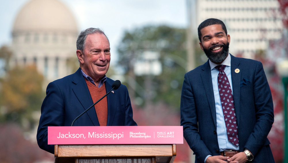 Jackson: 2 smiling men in suits, one at lectern.