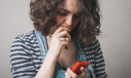 gun violence: Young woman looking at phone with concern, worry.