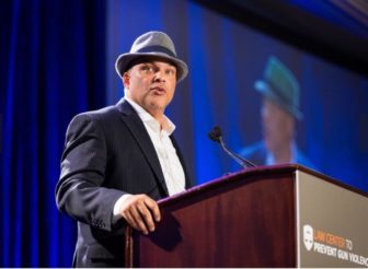 gun violence: DeVone Boggan (headshot), chief executive officer of Advance Peace, man in fedora, pinstriped suit at podium.