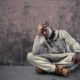 Chicago: Sad-looking young man of color with hand to head, sitting on ground.