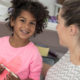 mentoring: Happy child in pink shirt with heart on it with adult with ponytail, rear view