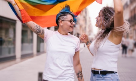 LGBTQIA+ community; Lesbian couple with playful attitude showing proudly a pride lgbt flag.