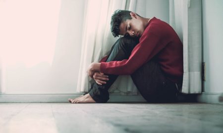 suicide: Youth sitting on floor next to curtain, head on knees