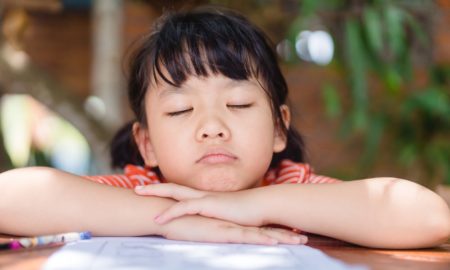 afterschool: Little girl with closed eyes rests chin on arms on table.