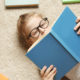 story county reads: young girl with blond hair and dark glasses reading blue book