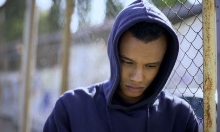 Too many locked doors report: young minority youth leaning sadly against chainlink fence