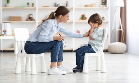 Early childhood mental health, youth health research grants: young woman therapist comforts a crying young boy sitting on small white chairs