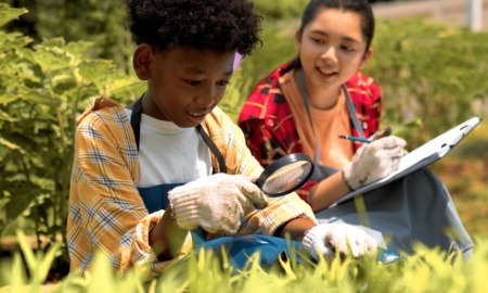 Gulf coast K-12 environmental education grants: black boy using magnifying glass to study among plants while Asian girl takes notes
