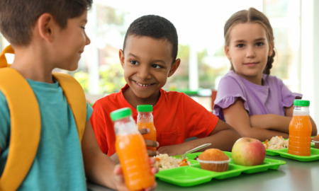 Summer EBT, summer meals in schools, school meals: Three elementary children sit at table with lime green trays eating lunch