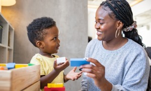 child care subsidy and industry: Black woman with long hair plays blocks with young black boy in child care setting