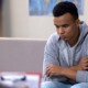 at-risk youth, Community-youth-violence-prevention: Black teen sullenly sits on couch across from counselor