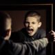 Severe irritability: Young male teen holds large mrror staring at own very angry reflection in dark room