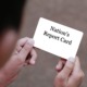 Nations Report Card: Closeup from back person's head over shoulder showing two hands holding small white card with black text "Nation's Report Card"