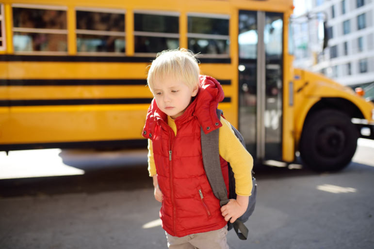 CHildren recovery after disaster: Young blonde boy with backpack walks away from yellow school bus