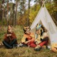 Camp Fire outdoor program interview: 3 young children wearing hand-made paper masks sit on the ground in front of a small tent in the woods